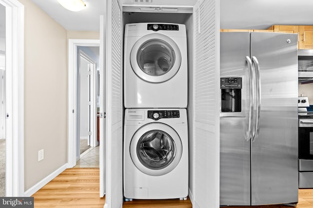 laundry room with baseboards, stacked washing maching and dryer, laundry area, and light wood-style flooring