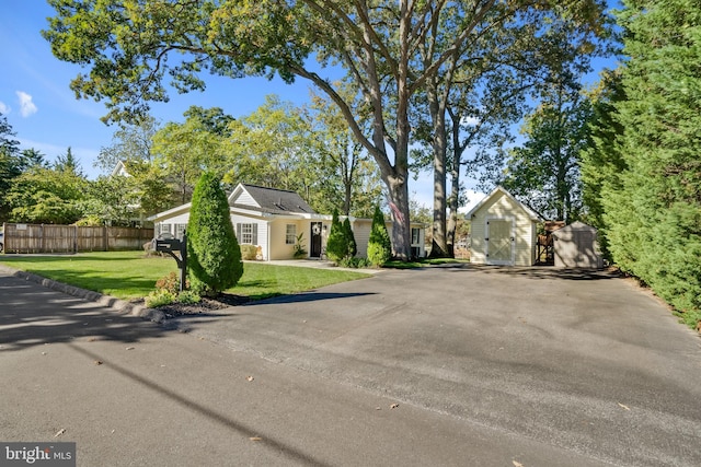 view of home's exterior featuring a yard, fence, aphalt driveway, an outbuilding, and a shed