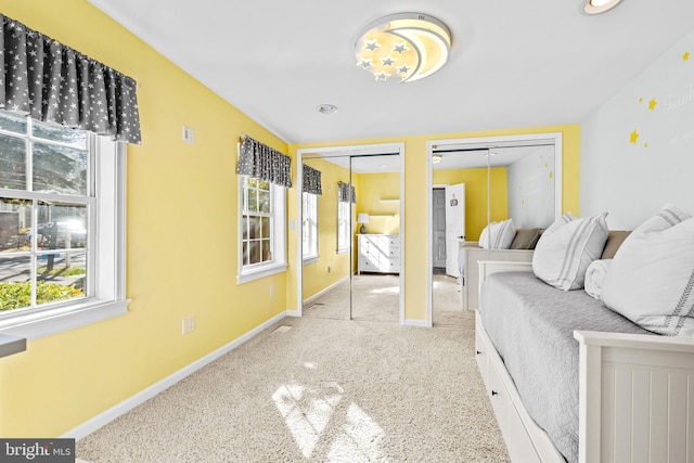 carpeted bedroom featuring baseboards, multiple windows, and two closets