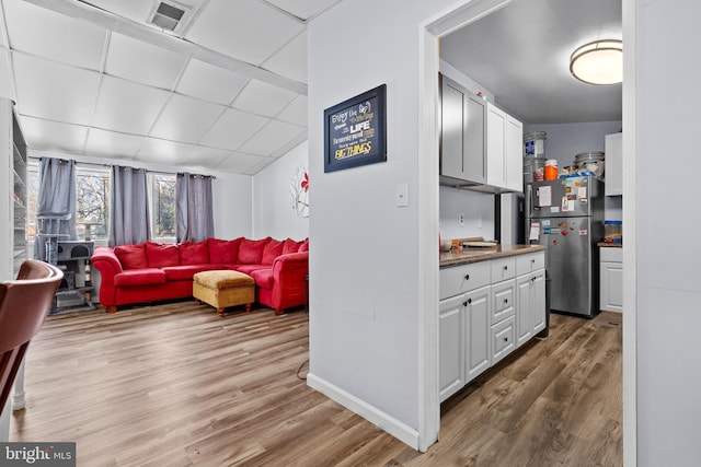 kitchen featuring light hardwood / wood-style floors, white cabinetry, a paneled ceiling, and stainless steel refrigerator