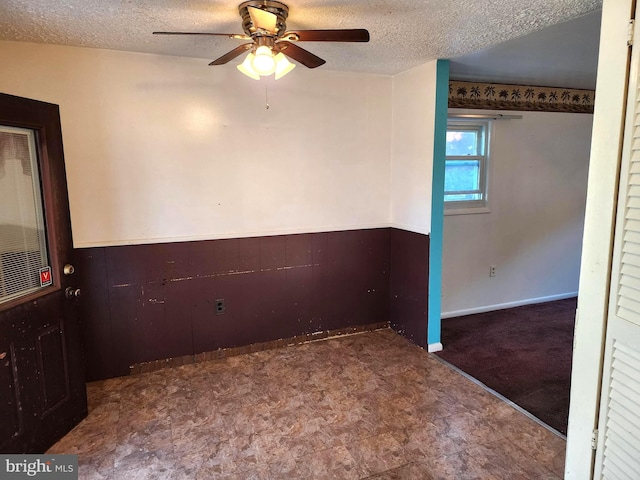 empty room featuring ceiling fan, a textured ceiling, and wooden walls