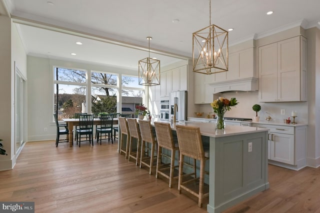 kitchen with an island with sink, crown molding, pendant lighting, light wood-type flooring, and high quality fridge