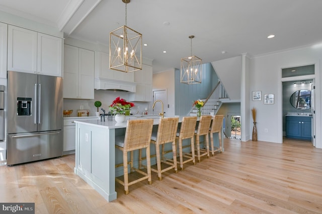 kitchen featuring stainless steel fridge with ice dispenser, white cabinetry, a kitchen island with sink, light wood-type flooring, and pendant lighting