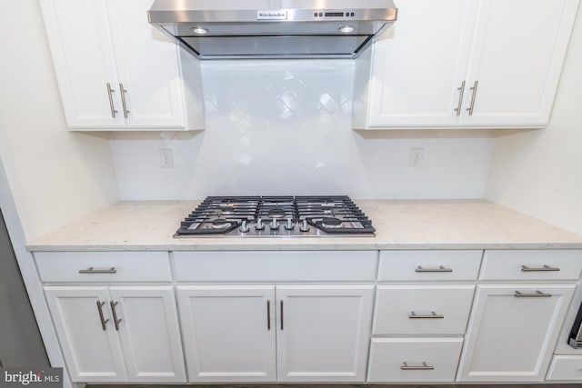 kitchen with ventilation hood, white cabinets, light stone counters, and stainless steel gas stovetop