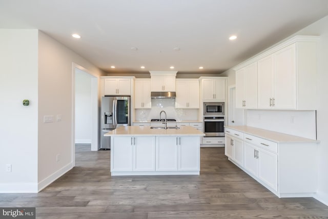 kitchen featuring an island with sink, tasteful backsplash, white cabinetry, appliances with stainless steel finishes, and hardwood / wood-style floors