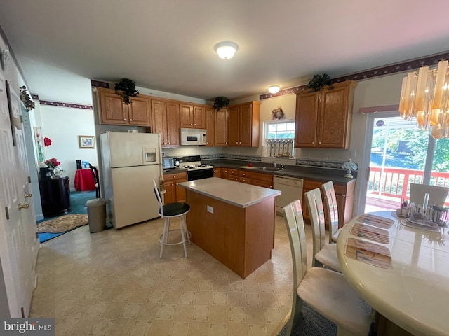 kitchen featuring a kitchen breakfast bar, white appliances, sink, a chandelier, and a center island