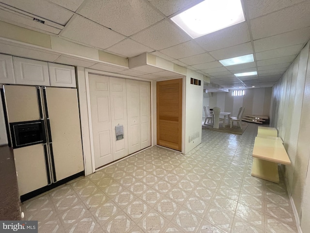 basement featuring a paneled ceiling and white fridge with ice dispenser