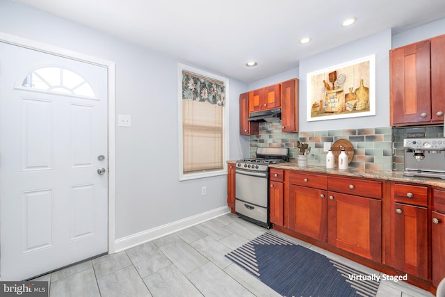 kitchen featuring stainless steel gas range oven, light stone counters, and backsplash