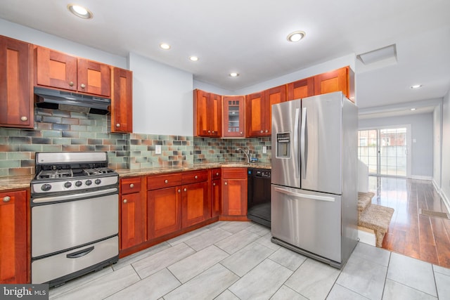 kitchen featuring light stone counters, decorative backsplash, stainless steel appliances, and light hardwood / wood-style flooring