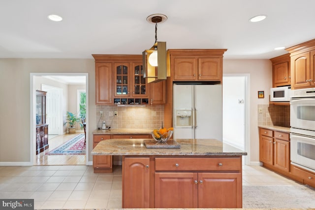 kitchen with white appliances, light stone countertops, a kitchen island, light tile patterned flooring, and tasteful backsplash