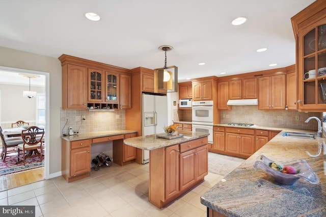 kitchen featuring white appliances, a center island, pendant lighting, light stone counters, and sink