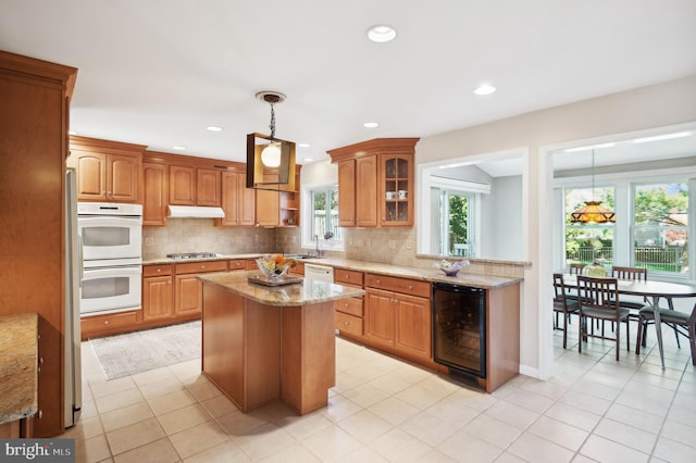 kitchen featuring wine cooler, hanging light fixtures, double oven, stainless steel gas stovetop, and a kitchen island