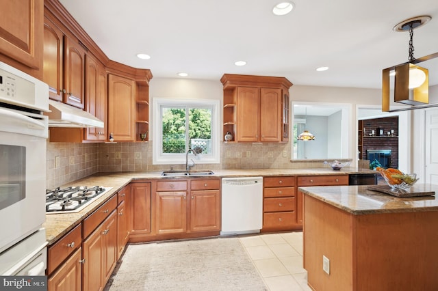 kitchen featuring white appliances, decorative light fixtures, light tile patterned floors, a brick fireplace, and sink