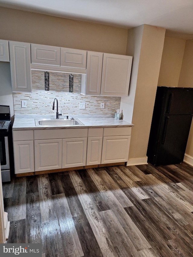 kitchen featuring sink, stainless steel stove, decorative backsplash, black refrigerator, and white cabinets