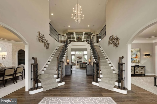 entryway featuring ornamental molding, dark wood-type flooring, a towering ceiling, and an inviting chandelier