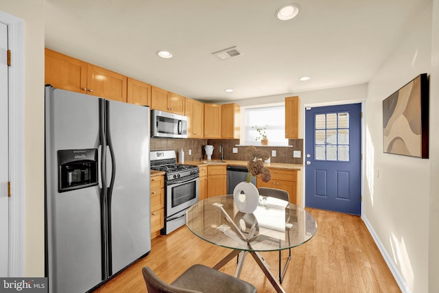 kitchen with stainless steel appliances, light brown cabinetry, tasteful backsplash, and light hardwood / wood-style flooring