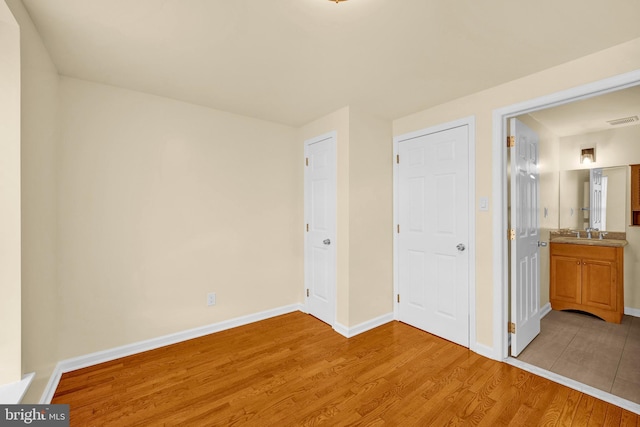 unfurnished bedroom with connected bathroom, sink, and wood-type flooring