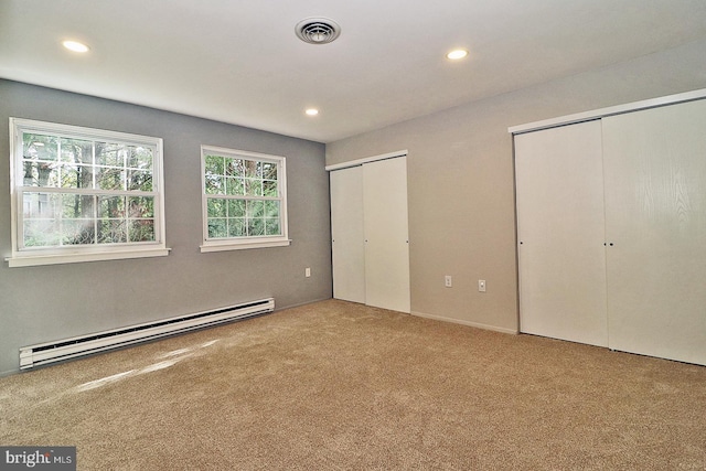 unfurnished bedroom featuring baseboard heating, two closets, and carpet flooring