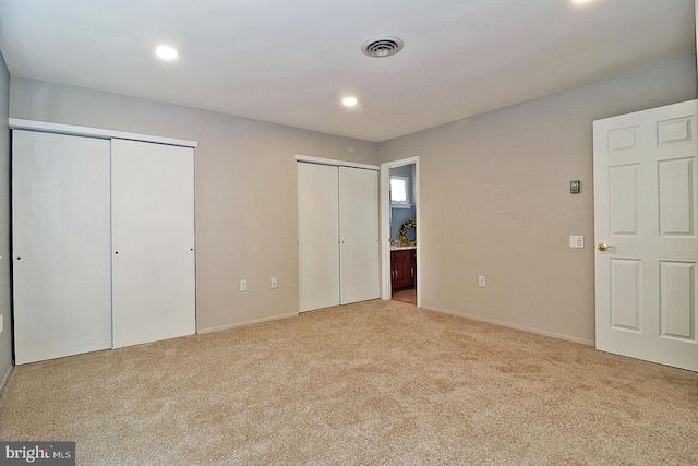 unfurnished bedroom with light colored carpet, ensuite bathroom, and multiple closets