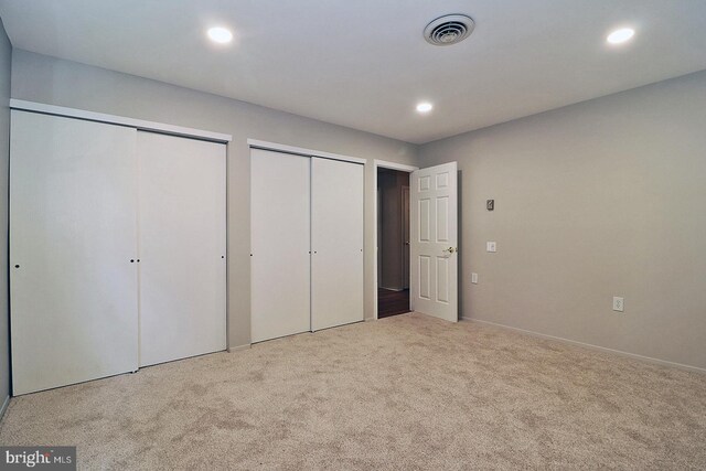 unfurnished bedroom featuring light colored carpet and two closets