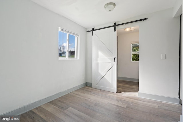 unfurnished room featuring a wealth of natural light, a barn door, and light hardwood / wood-style floors