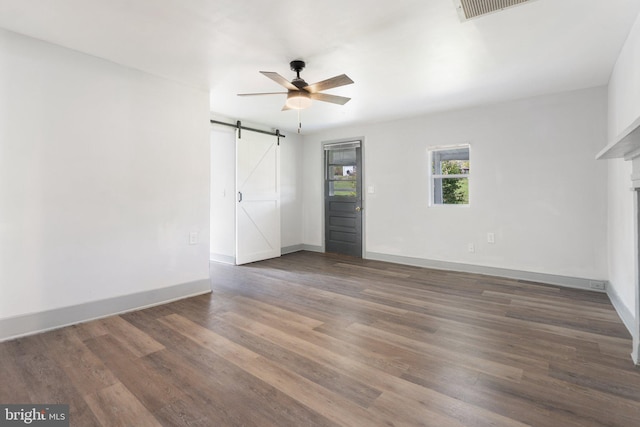 unfurnished room with a barn door, ceiling fan, and dark hardwood / wood-style flooring