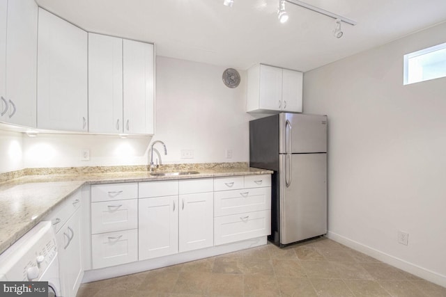 kitchen with washer / clothes dryer, sink, white cabinets, light stone counters, and stainless steel refrigerator