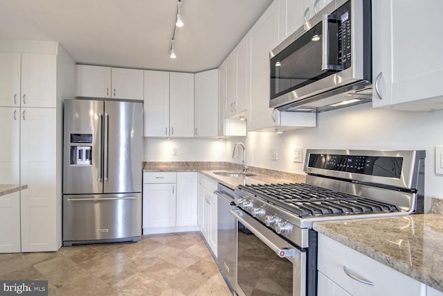 kitchen featuring white cabinets, light stone counters, rail lighting, sink, and stainless steel appliances