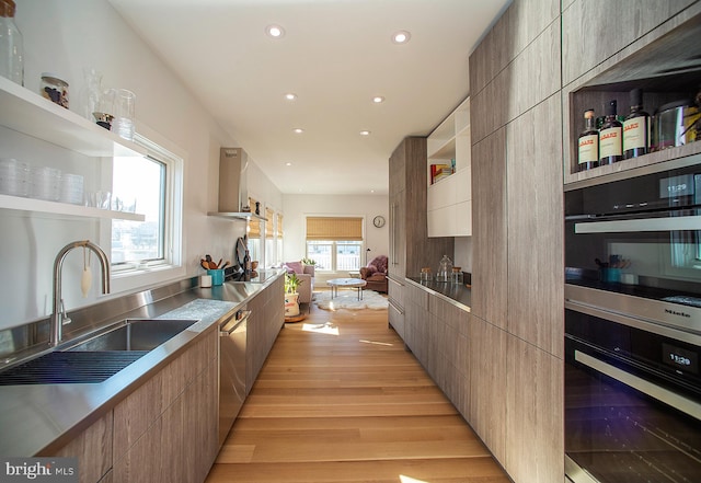 kitchen featuring wall chimney range hood, stainless steel counters, light hardwood / wood-style flooring, dishwasher, and sink