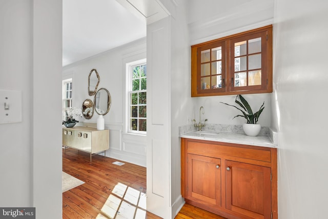 bar with ornamental molding, sink, and light hardwood / wood-style flooring