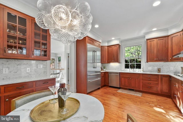 kitchen featuring a notable chandelier, stainless steel appliances, ornamental molding, and light hardwood / wood-style flooring