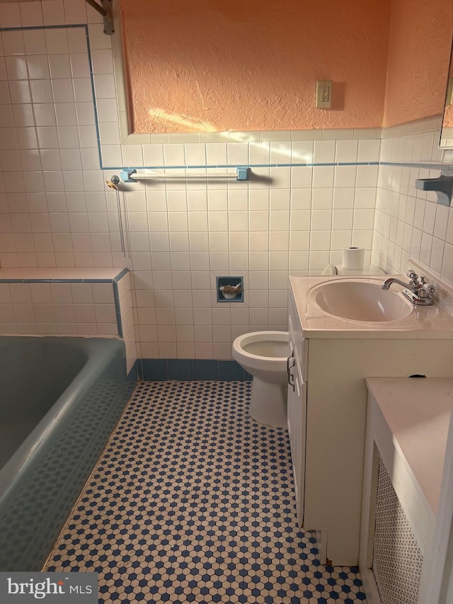 bathroom featuring a tub to relax in, vanity, tile walls, and toilet