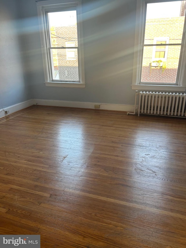 empty room with plenty of natural light, dark hardwood / wood-style floors, and radiator