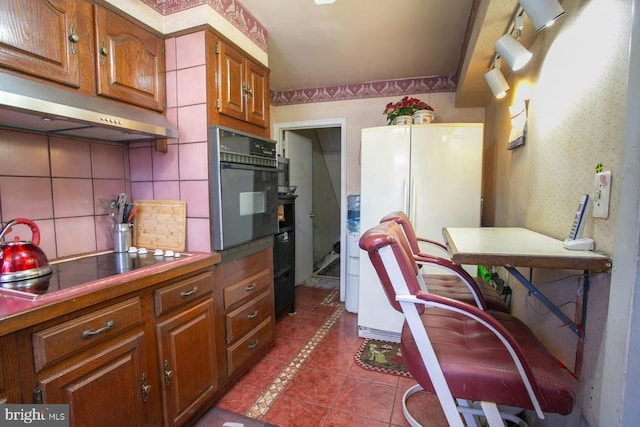 1144 E Slocum St, Philadelphia, PA 19150 - kitchen with black appliances, under cabinet range hood, tile counters, brown cabinetry, and tasteful backsplash