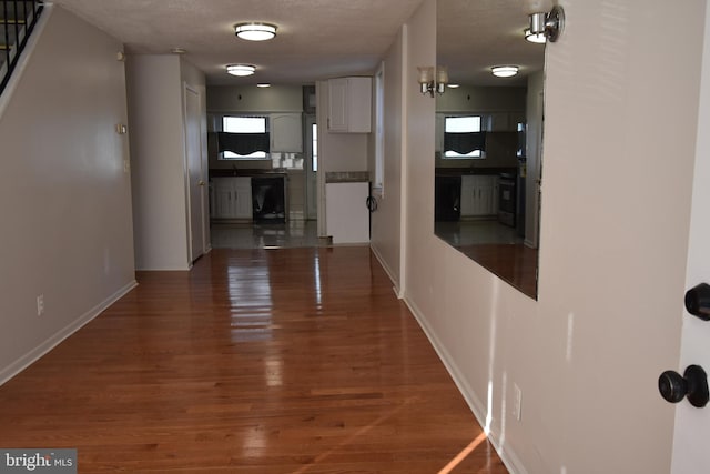 corridor with a wealth of natural light, a textured ceiling, and dark hardwood / wood-style flooring