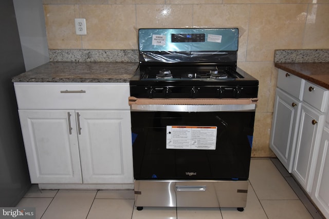 kitchen featuring refrigerator, light tile patterned floors, white cabinetry, stainless steel range oven, and tasteful backsplash