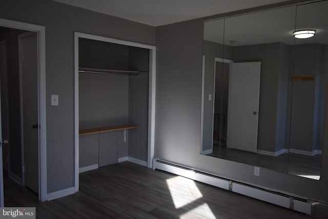 unfurnished bedroom with a closet, a baseboard heating unit, and dark hardwood / wood-style flooring