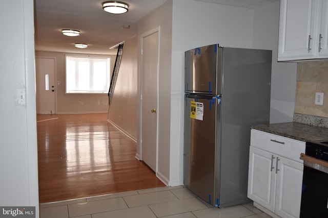 kitchen featuring white cabinetry, dark stone countertops, stainless steel refrigerator, and light wood-type flooring