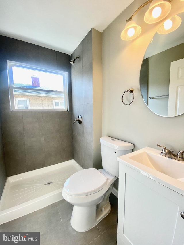 bathroom with toilet, vanity, tile patterned floors, and tiled shower