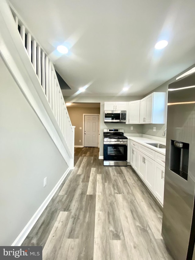 kitchen with appliances with stainless steel finishes, sink, light wood-type flooring, and white cabinets