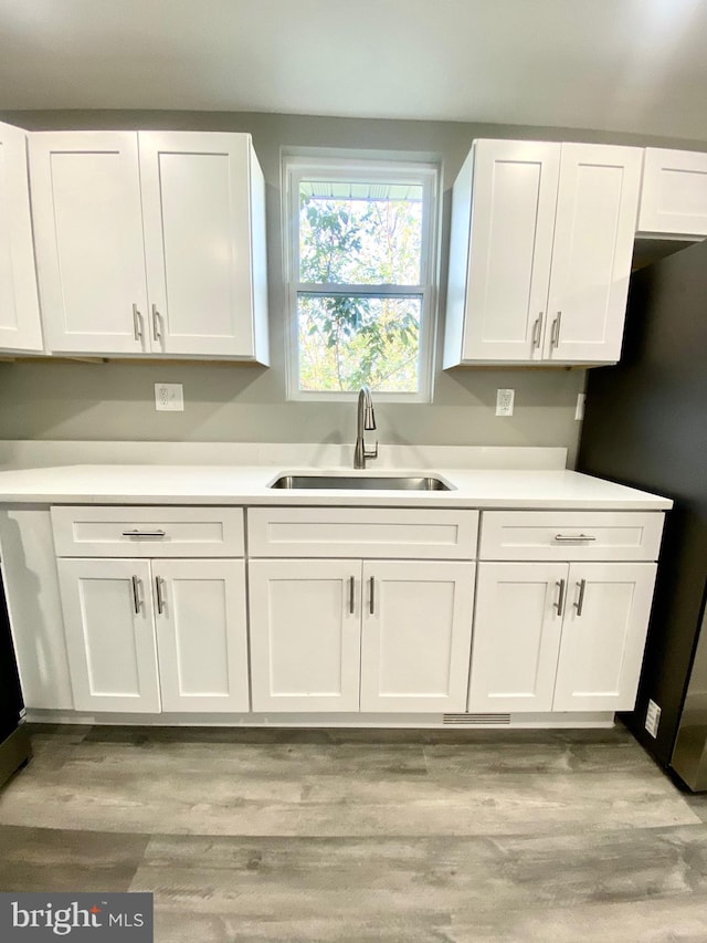 kitchen with light hardwood / wood-style floors, white cabinets, sink, and stainless steel refrigerator