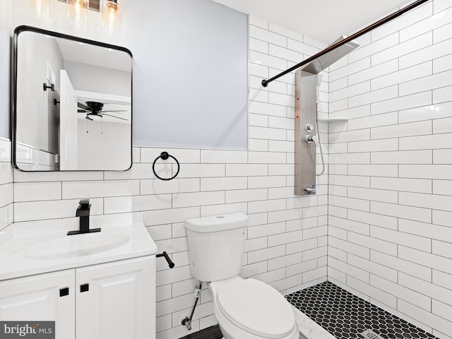 bathroom featuring vanity, toilet, a tile shower, and tile walls