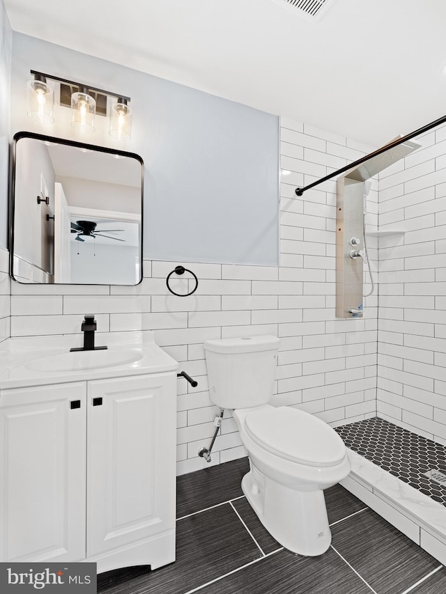 bathroom featuring tile walls, tile patterned floors, tiled shower, vanity, and toilet