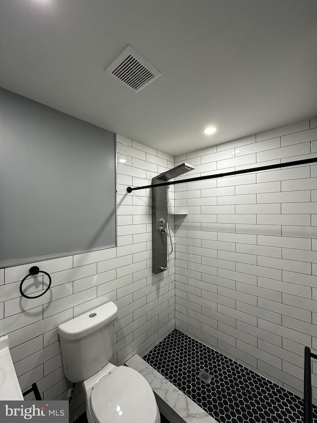 bathroom with tile walls, tiled shower, and toilet