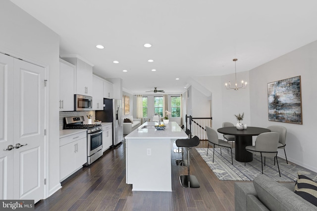 kitchen with a kitchen island with sink, dark wood-type flooring, sink, decorative light fixtures, and appliances with stainless steel finishes