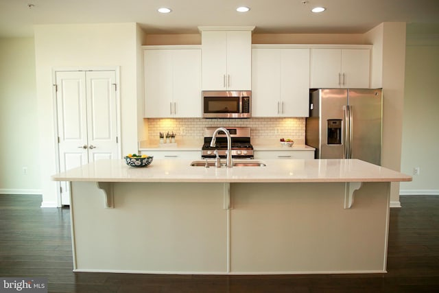 kitchen featuring dark hardwood / wood-style flooring, white cabinetry, stainless steel appliances, and an island with sink