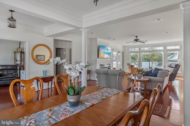 dining room featuring ornate columns, hardwood / wood-style flooring, ornamental molding, a fireplace, and ceiling fan