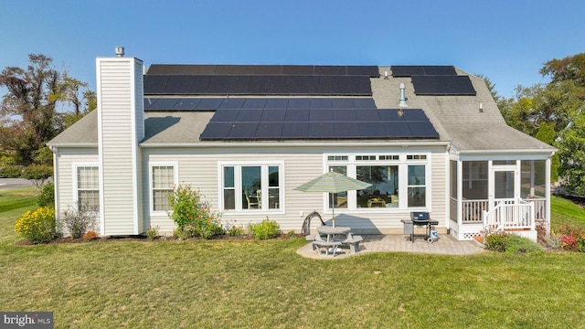 rear view of property with a yard, a patio area, a sunroom, and solar panels