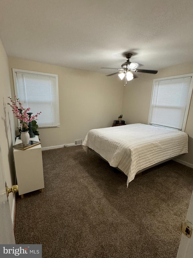 bedroom featuring ceiling fan, a textured ceiling, and dark colored carpet