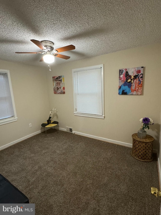 empty room with ceiling fan, a textured ceiling, and dark colored carpet